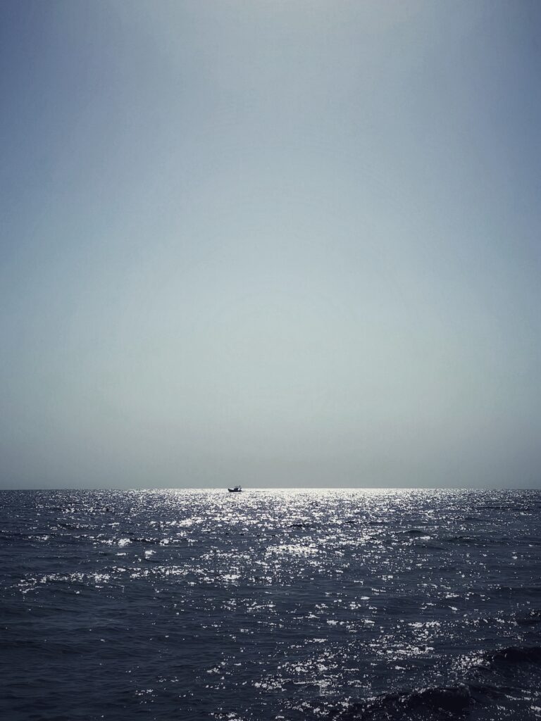 Sonnenlicht glitzert auf dem weiten Meer, ein kleines Boot am Horizont.