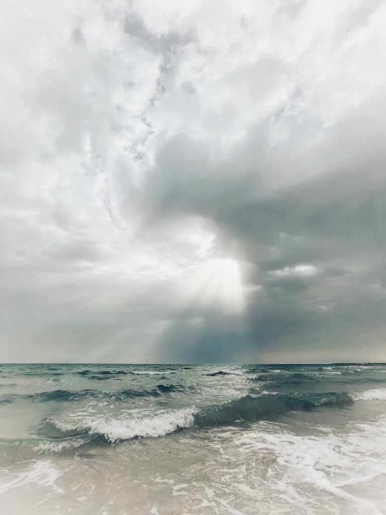Sonnenstrahlen brechen durch dichte Wolken über dem aufgewühlten Meer.