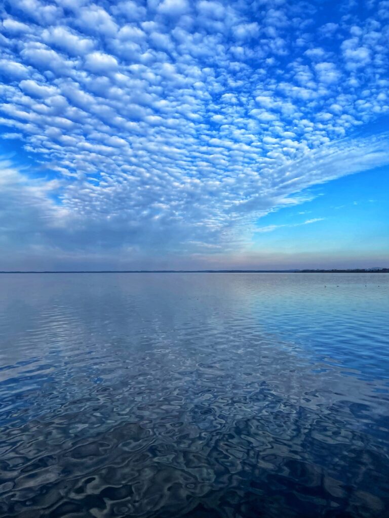 Weite Wolkenformation über ruhigem See mit Spiegelungen im Wasser.